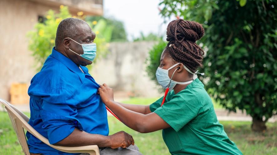 Nurse helping a senior man outside, both wearing masks.