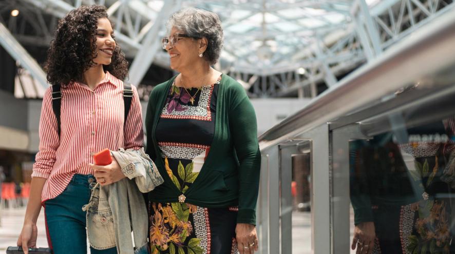 Young woman with curly brown hair and striped shirt walking with older woman with short grey hair in airport